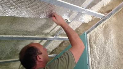 מתקין מצמיד יריעת בידוד רפלקטיבית לקונסטרוקציית מתכת בעליית גג עם קצף מוקצף קיים